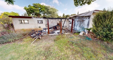 בית הרוס בקיבוץ רעים לאחר מתקפת השביעי באוקטובר. חזית המבנה קרסה, חלונות מנופצים וגג פגוע. ערימות של הריסות וחפצים מפוזרים מציגים את עוצמת הנזק. התמונה משמשת כתיעוד היסטורי של הפגיעה בקיבוץ כחלק מתהליך השיקום במסגרת תקומה.